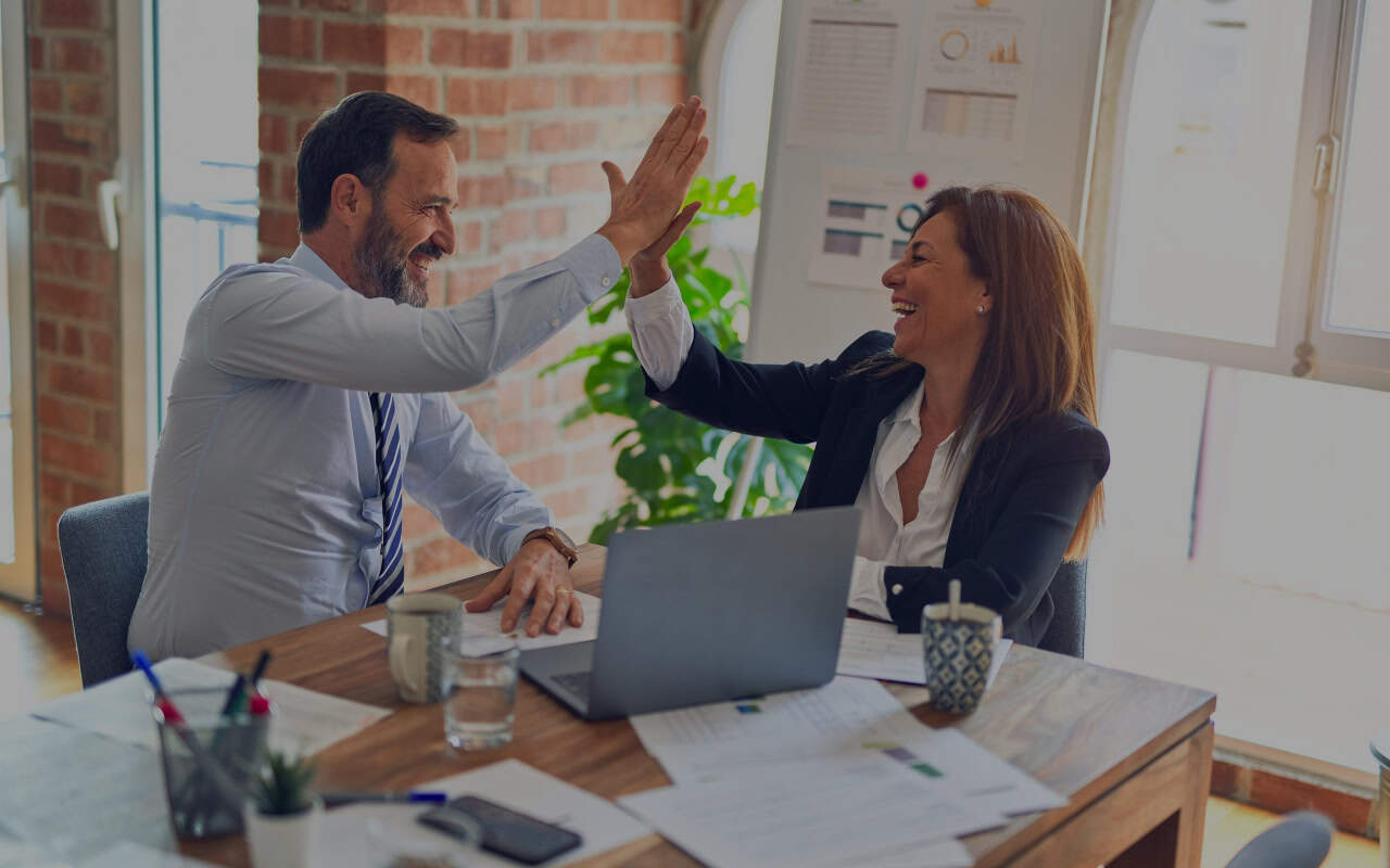 two people laughing and high fiving at an office table