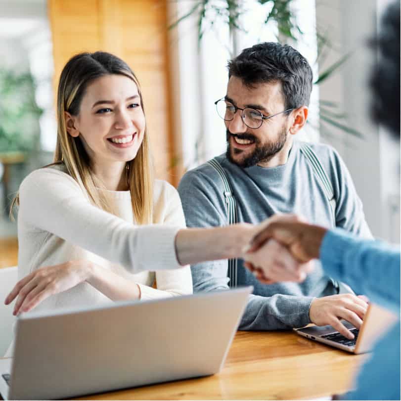 Happy young man and woman shaking hands over a computer during insurance career training